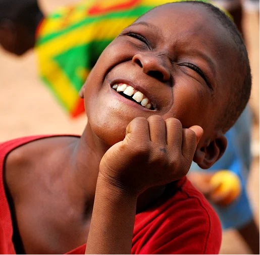 A joyful boy in a red shirt grins widely, showcasing his teeth and expressing happiness.