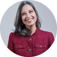 Smiling woman with long gray hair, wearing a red jacket with buttons, against a light gray background.