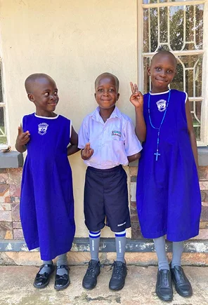 Three children in bright purple school uniforms smile and pose together outdoors.