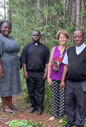 Four people standing in a wooded area, dressed in casual and formal attire, smiling at the camera.