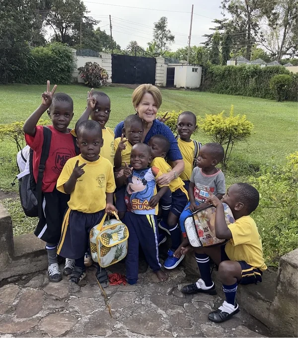 A group of smiling children in yellow shirts pose with an adult in an outdoor setting.
