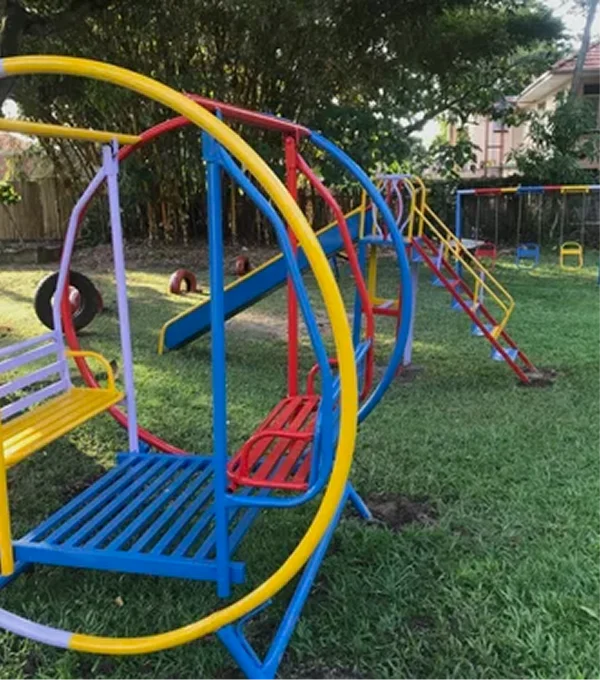 Colorful playground equipment, including slides and climbing structures, set on grass in a sunny outdoor area.