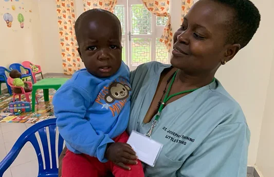 A caregiver holds a young child in a brightly colored room filled with toys and playful decorations.