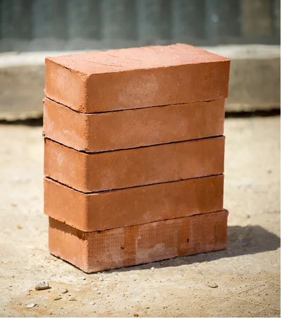 Stack of four red bricks placed on sandy ground.