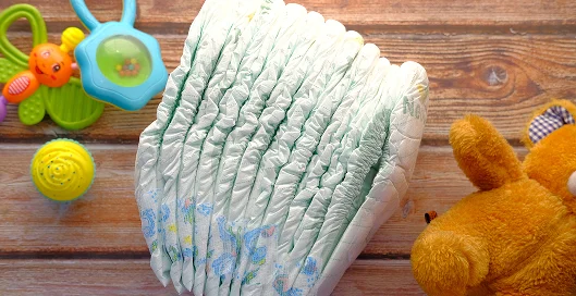 A stack of diapers beside colorful toys on a wooden surface.